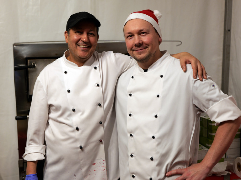 Zwei Köche der Albertinen Services Hamburg in weißen Kochschürzen blicken fröhlich in die Kamera bei der Weihnachtsfeier 2025 von Amalie Sieveking Krankenhaus, Residenz am Wiesenkamp, Feierabendhaus Volksdorf und Albertinen Kindertagesstätte Volksdorf auf dem Gesundheitscampus Volksdorf in Hamburg