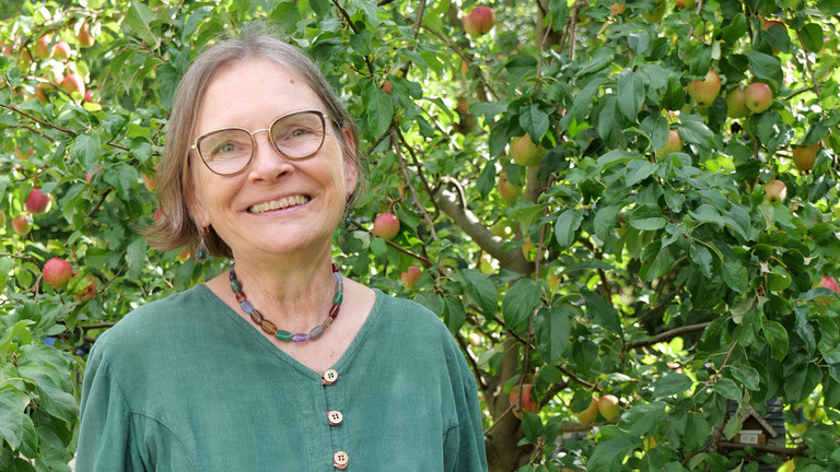 Mirjam Ritz steht lächelnd vor einem Apfelbaum