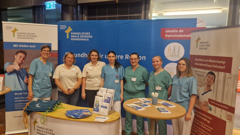 Sieben Mitarbeiterinnen der Hamburger Einrichtungen der Immanujel Albertinen Diakonie stehen nebeneinander an einem Stand auf der Berufsorientierungsmesse